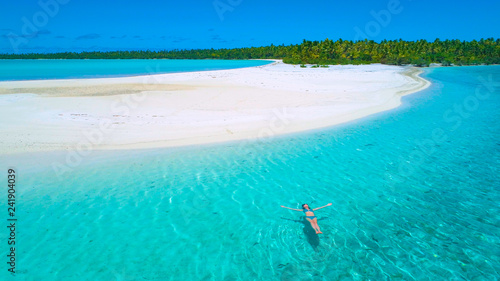 AERIAL: Flying close to young woman swimming on her back close to sandy beach.