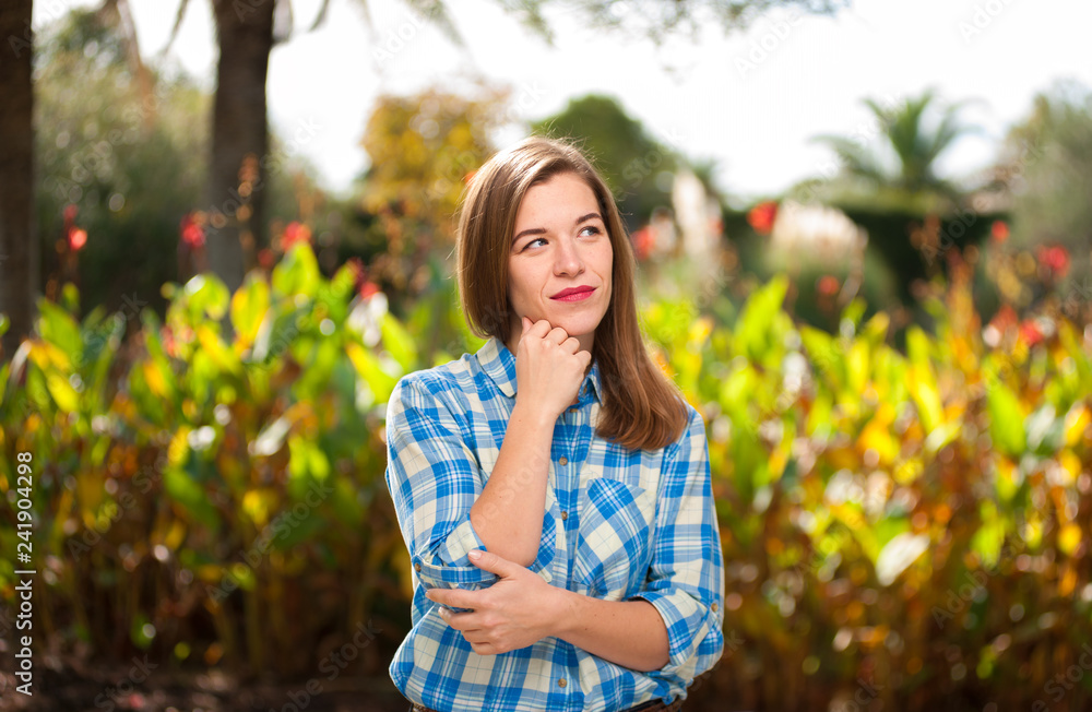Naklejka premium Beautiful young smiling girl posing against blurry summer trees on sunny day