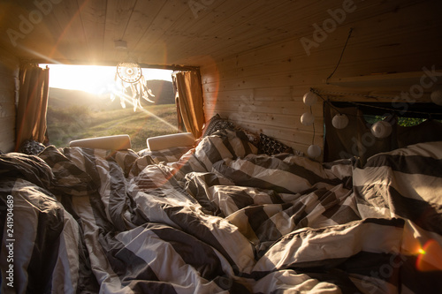 Interior of camper van with cozy bed during summer sunset