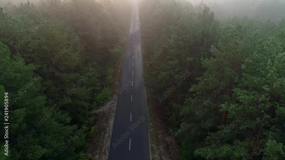 Aerial view of people running along the asphalt road between a forest with fog and sunrise. Concept: running, fitness, healthy lifestyle, well-being, marathon Aerial view of people running along the asphalt road between a forest with fog and sunrise. Concept: running, fitness, healthy lifestyle, well-being, marathon