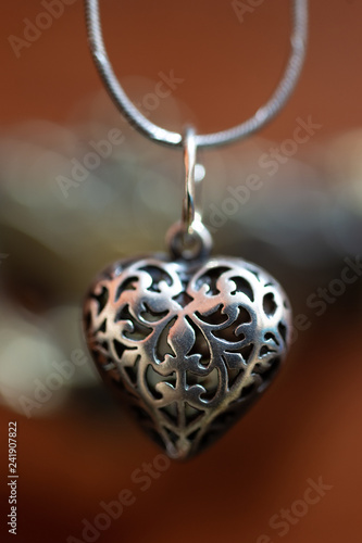 Close up photo of female neck silver pendand on blurred background. A handwork sterling silver pendant look as heart. Macrophoto with blurred background. photo