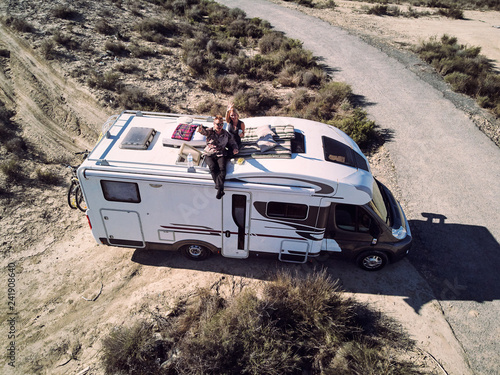 Fototapeta Couple sitting at camper car roof and waving hands