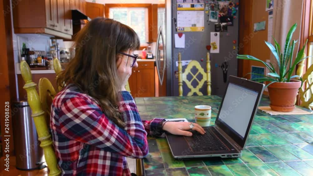 Woman at the table working with laptop. Girl with glasses wearing a checkered shirt is typing on her keyboard, then gets discouraged. Fixed wide angle scene Woman at the table working with laptop. Girl with glasses wearing a checkered shirt is typing on her keyboard, then gets discouraged. Fixed wide angle scene