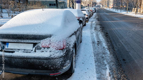 In the street side parked cars covered with snow.