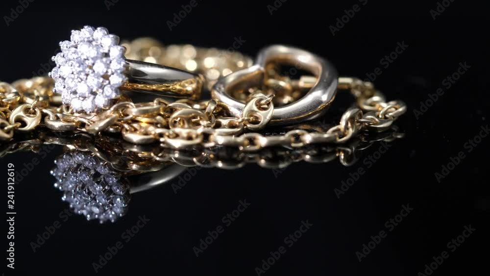 Schwenk über Goldkette mit Herz und Brilliantring gespiegelt auf schwarzer Acrylplatte Schwenk über Goldkette mit Herz und Brilliantring gespiegelt auf schwarzer Acrylplatte