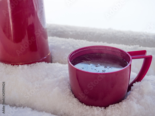Thermos and cup of tea with lemon on bench covered with snow