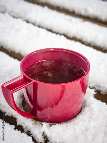 Plastic cup of tea with lemon on bench covered with snow