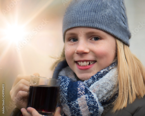 Mädchen hält glücklich einen Kinderpunsch als warmes Getränk auf einem Weihnachtsmarkt