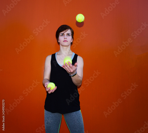 Young sporty girl juggling balls on orange background.