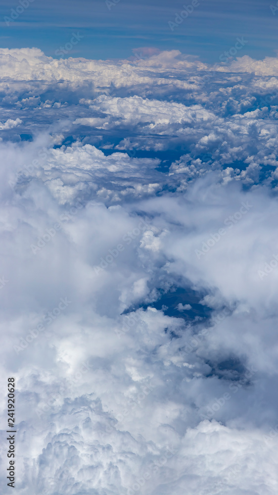 Beautiful view from window of plane flying over clouds. Natural panorama with clouds. White clouds moving above the ground. 