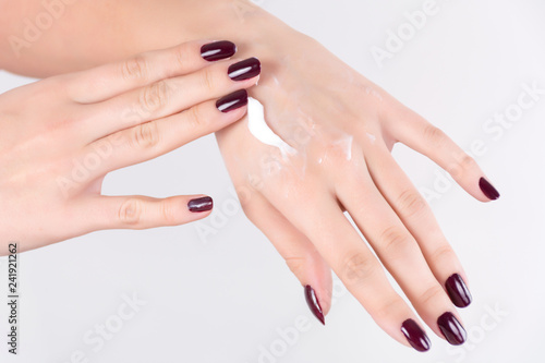 Young girl applying hand cream on skin and girl has red wine nails polish gel  isolated on white background. Female beauty  manicure and cosmetics concept. Close up  selective focus.