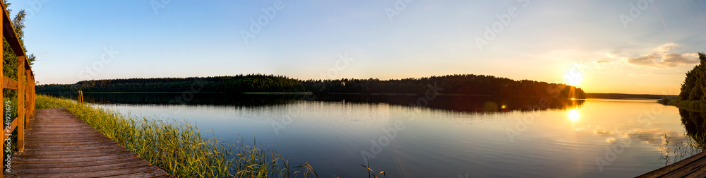 ein Panorama von einem See umgeben von Wald bei Sonnenuntergang - obrazy, fototapety, plakaty 