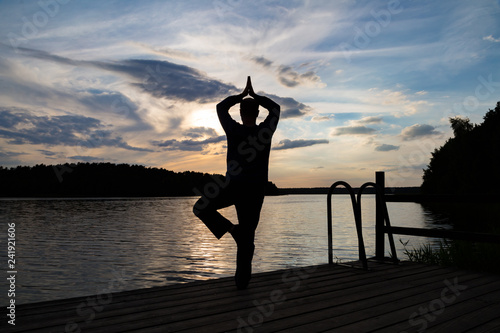 ein Mann steht bei Sonnenuntergang am See und macht Sport