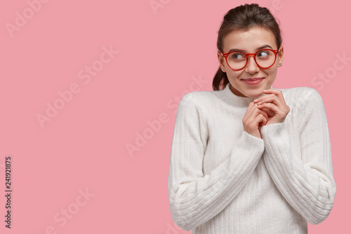Optimistic dreamy young woman keeps hands together, focused aside with gentle...