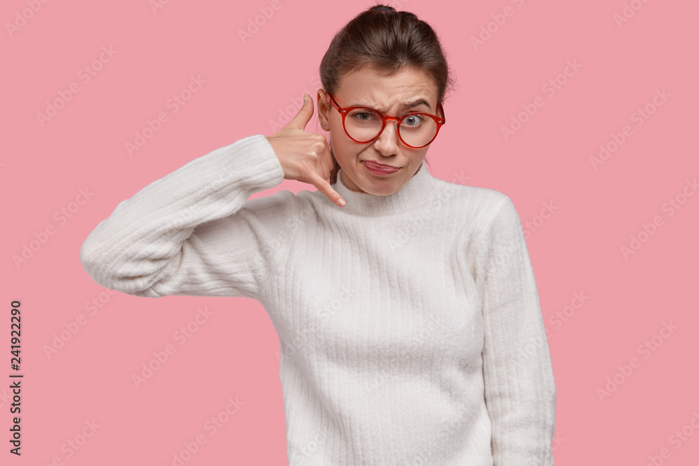 Photo of dissatisfied woman makes call gesture, asks boyfriend call back, gestures on distance, frowns face, dressed in white clothes, models over pink studio wall. Lady pretends holds cell phone Photo of dissatisfied woman makes call gesture, asks boyfriend call back, gestures on distance, frowns face, dressed in white clothes, models over pink studio wall. Lady pretends holds cell phone