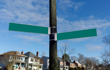 Blank street signs with neighborhood housing under blue sky. Copy space.