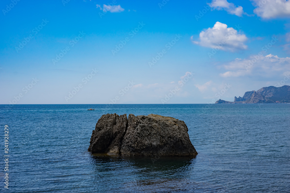 Seascape with a large rock in the sea under the blue sky.