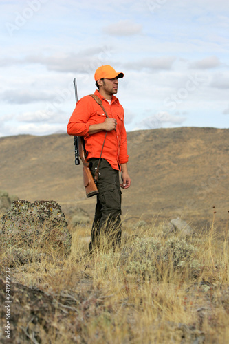 An adult male big game hunter in the mountains holding a large caliber rifle.