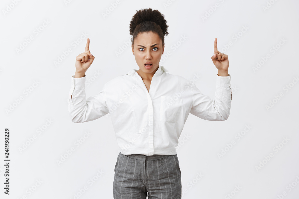 What the heck. Portrait of displeased confused african-american female with bun hairstyle in white shirt and pants, staring questioned and disappointed at camera while pointing up with raised hands What the heck. Portrait of displeased confused african-american female with bun hairstyle in white shirt and pants, staring questioned and disappointed at camera while pointing up with raised hands