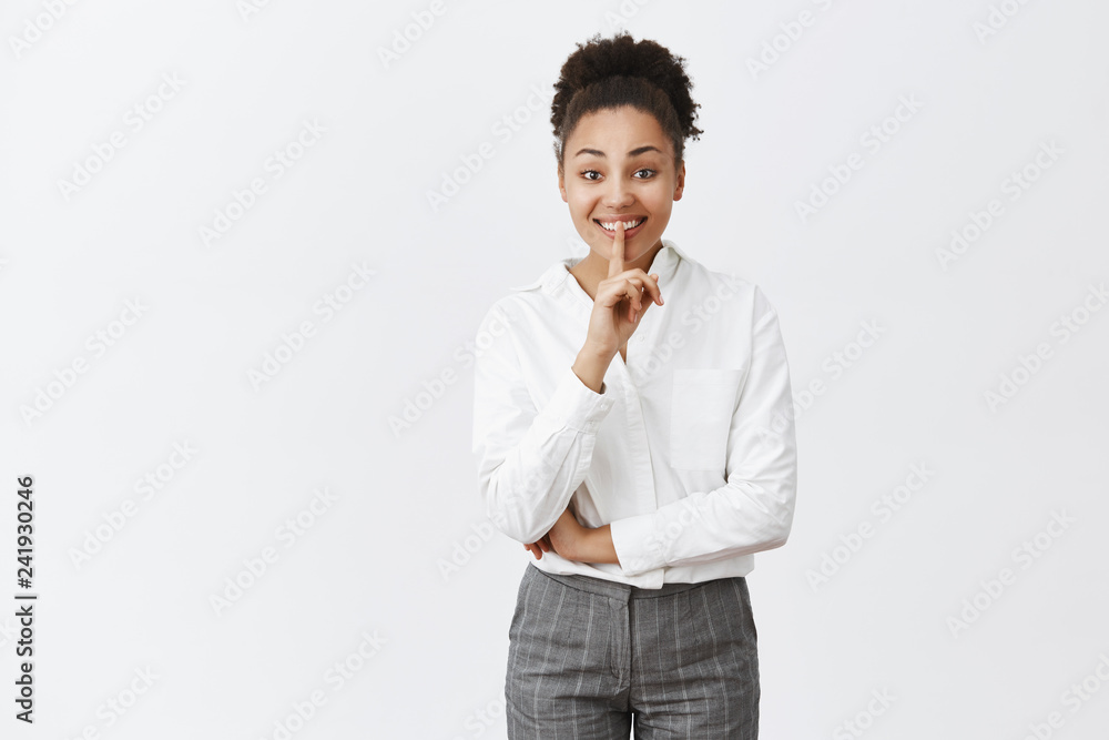 Shhh, no words please. Portrait of charming friendly-looking dark-skinned woman with curly hair in suit, keeping secrets, showing shush gesture with index finger over mouth, smiling from happiness Shhh, no words please. Portrait of charming friendly-looking dark-skinned woman with curly hair in suit, keeping secrets, showing shush gesture with index finger over mouth, smiling from happiness