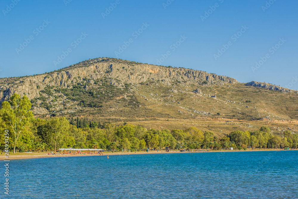 summer sea vacation and people on sand beach in bay surrounded by mountain on blue sky background 