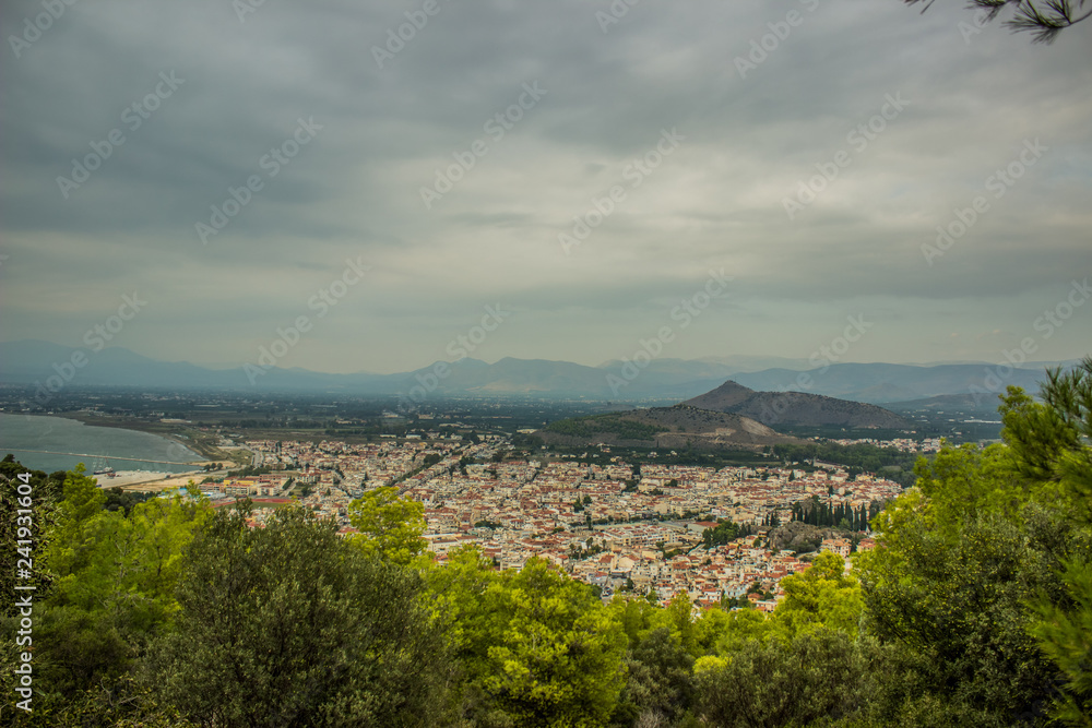 aerial city photography with trees tops in foreground and small European town in big valley near sea surrounded by mountain in gray cloudy rainy day