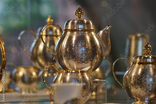 Silver teapot with blackened floral patterns on blurred background.