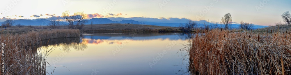 Views of Josh’s Pond walking path, Reflecting Sunset in Broomfield Colorado surrounded by Cattails, plains and Rocky mountain landscape during sunset. United States.