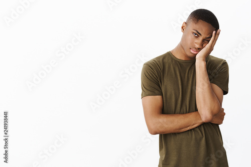 Guy hates long queues. Bored and indifferent attractive young african american male making face palm, leaning head on hand peeking with one eye at camera apathic and tired over white background photo