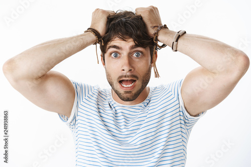 Worried and panicking young confused guy with blue eyes pulling hair out of head and open mouth feeling anxious and scared as realising girlfriend got pregnant being scared of responsibilities photo