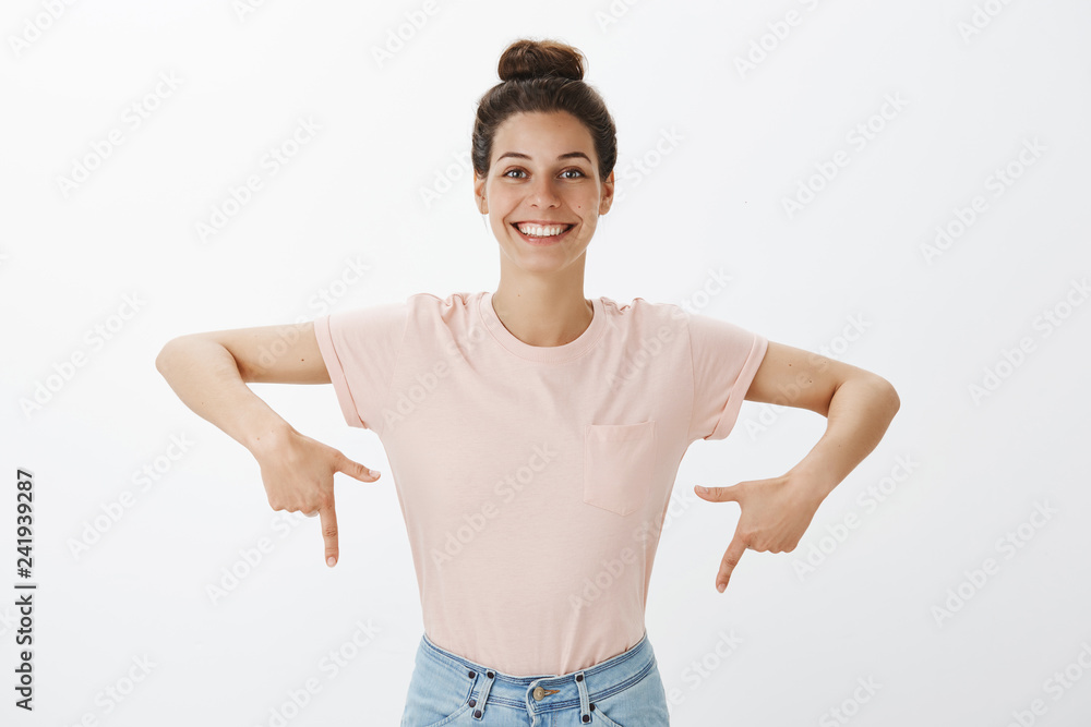 Waist-up shot of cheerful bright and happy charismatic beautiful european female with nice cheerful smile pointing down with raised fingers as showing proudly project she made over gray wall Waist-up shot of cheerful bright and happy charismatic beautiful european female with nice cheerful smile pointing down with raised fingers as showing proudly project she made over gray wall