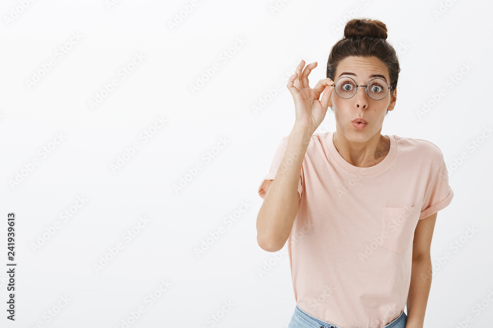 Girl putting on glasses realising how world look without blur folding lips bending towards camera amused and impressed standing excited and speechless with astonished expression over gray background Girl putting on glasses realising how world look without blur folding lips bending towards camera amused and impressed standing excited and speechless with astonished expression over gray background