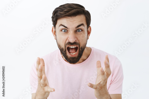 Pissed guy yelling from anger and hate during argument. Portrait of outraged pressured caucasian male with beard screaming and gesturing with itense hands with hate and disgust over white background photo