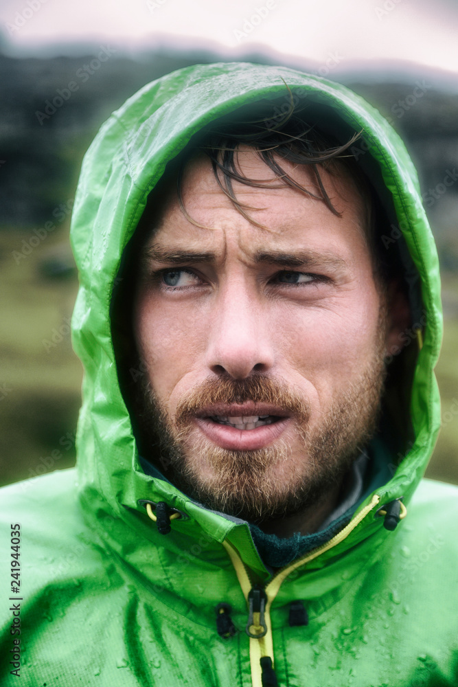 Hiker man on extreme hike adventure outdoor raining wearing waterproof rain jacket hood. Portrait of rugged scandinavian young adult sportsman outside. Hiker man on extreme hike adventure outdoor raining wearing waterproof rain jacket hood. Portrait of rugged scandinavian young adult sportsman outside.