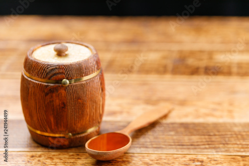 Closed keg with honey and wooden spoon on a wooden table. Barrel.