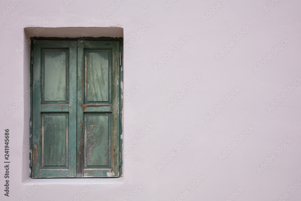 Old fashioned worn window with green wooden shutters, closed, on painted wall background. Old fashioned worn window with green wooden shutters, closed, on painted wall background.