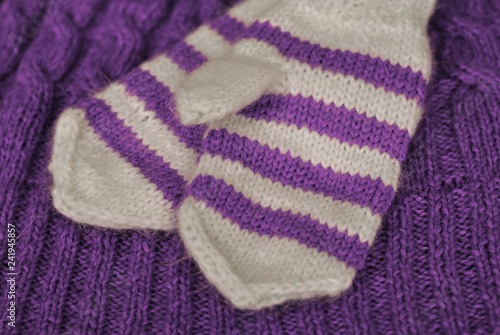 Knit. Homemade knitted striped mittens on knitted pattern background. Purple color.