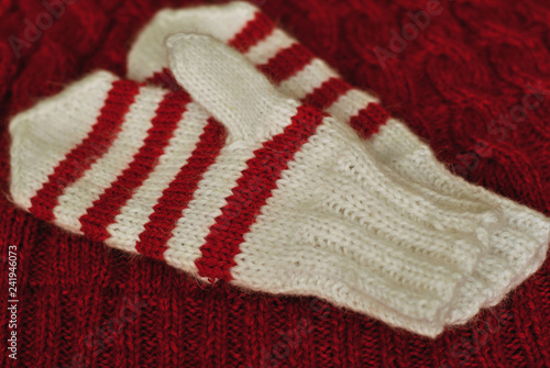Knit. Homemade knitted striped mittens on knitted pattern background. Red color.