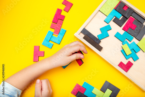 Wooden puzzle and kids hands on yellow background. Flat lay photo