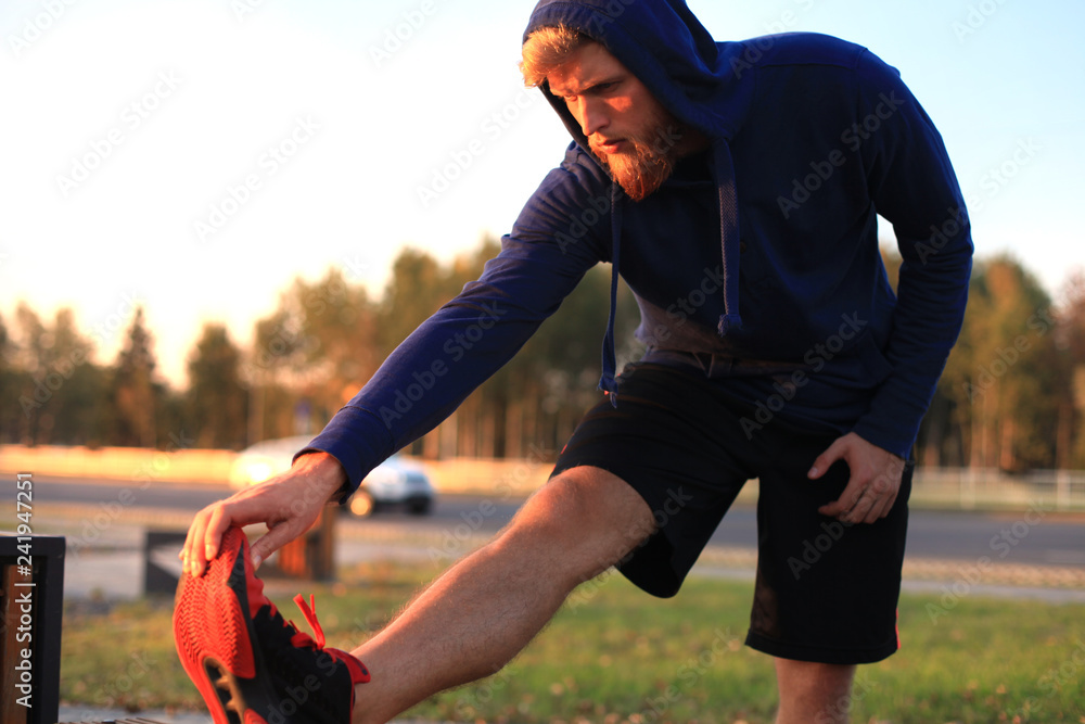 Fototapeta premium Handsome young man doing stretching exercises before running while standing outdoors.