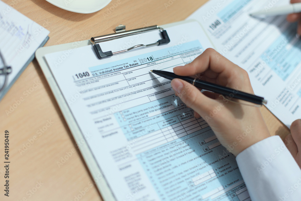 Woman filling in U.S. Individual income tax return, tax 1040 at table. Woman filling in U.S. Individual income tax return, tax 1040 at table.