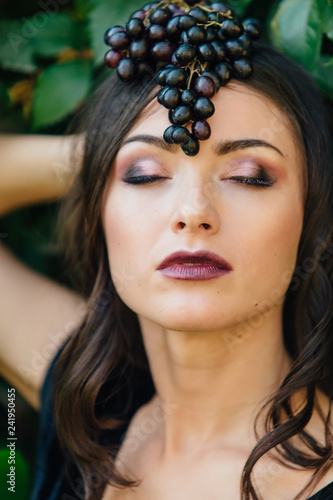 Portrait of young sexy brunette with black grapes on head.