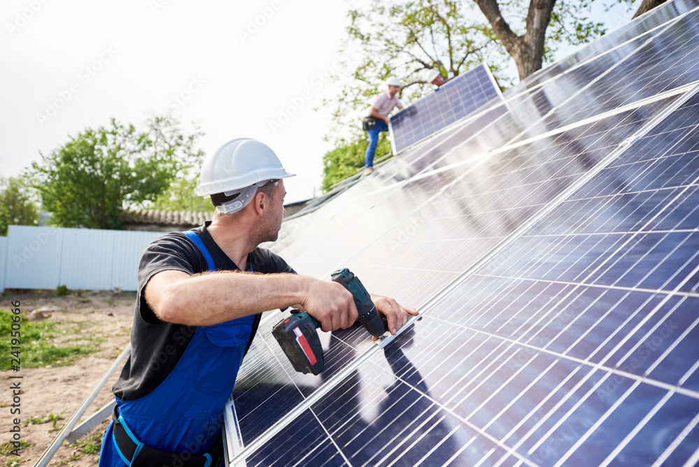 Engineer technician connecting solar photo voltaic panel using screwdriver with team of workers on metal platform. Stand-alone solar system installation, efficiency and professionalism concept. Engineer technician connecting solar photo voltaic panel using screwdriver with team of workers on metal platform. Stand-alone solar system installation, efficiency and professionalism concept.