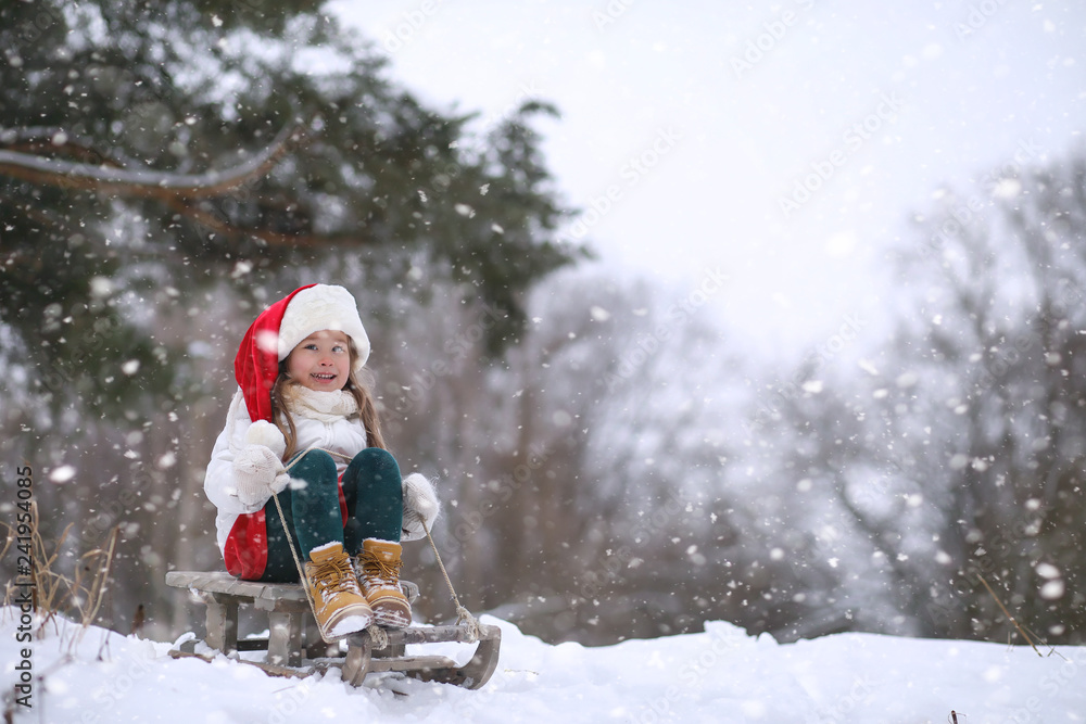 A winter fairy tale, a young mother and her daughter ride a sled in the forest. A girl on a sled with gifts on the eve of the new year in the park.