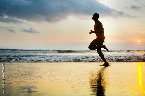 silhouette of young attractive fit athletic and strong black afro American man running at sunset beach training hard and sprinting on sea water runner workout