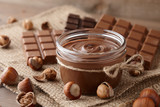 Chocolate spread or nougat cream with hazelnuts in glass jar on wooden background
