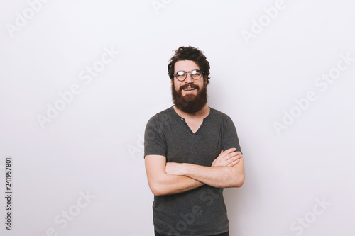 Happy smiling bearded man with crossed hands standing over white wall