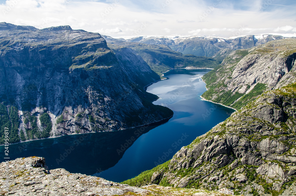 Spectacular view of a blue lake 700 meters lower under the Trolltunga rock and interesting sky with few clouds