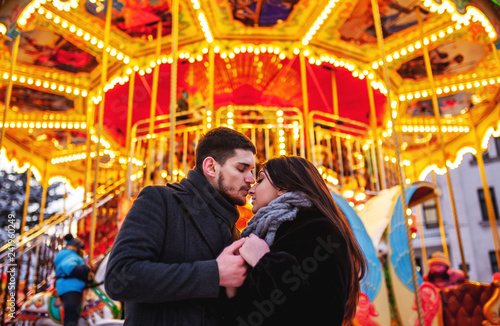 young couple standing near the bright carousel, cuddles and kisses,concept of joint rest © александр таланцев
