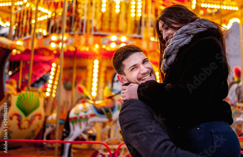 young couple standing near the bright carousel  cuddles and kisses concept of joint rest